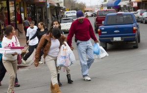 After finishing a shopping trip in Nogales, Ariz., a family with handfuls of shopping bags walks toward the border to return to Mexico. An increase in the Mexico sales tax has many families traveling across the border to do their shopping. (Photo by Kyle Mittan)