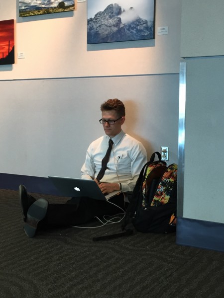 Zachary Bramble, an employee of Enterprise car rentals, sits on the floor of the Tucson International Airport while he charges his laptop. Photo by: Megan Mohler/ Arizona Sonora News Service