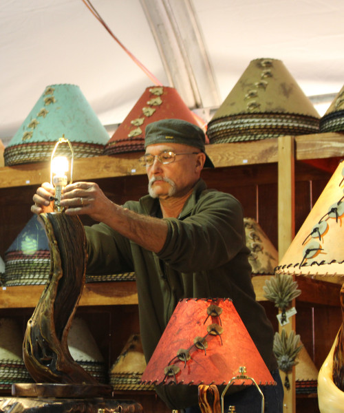 Chris Jafferis, a designer and co-owner of Sticks n Stones, adjusts a lightbulb on one of his wooden lamps at the Kino Gem & Mineral Show, a part of the Tucson Gem, Mineral and Fossil Showcase in Tucson, Ariz. on Feb. 3, 2016. Jafferis cuts the wood pieces himself, and said each lamp is "one of a kind." (Photo by Maggie Driver)