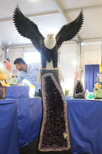 An eagle sculpture by artist Daniel Venturini, pictured in background, at the JG&M Expo at the Tucson Gem, Mineral & Fossil Showcase on Jan. 30, 2016. Venturini said the sculpture, which is perched atop an Amethyst geode, took two months to complete. (Photo by Maggie Driver)