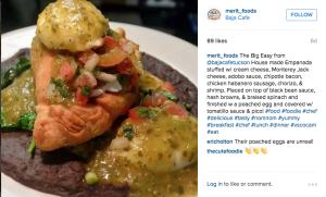 An Instagram post by @merit_foods from February 2016 shows a house-made empanada from Baja Cafe with Monterey Jack cheese, bacon, chicken habanero sausage, chorizo, shrimp, black bean sauce, hash browns, braised spinach and a poached egg.