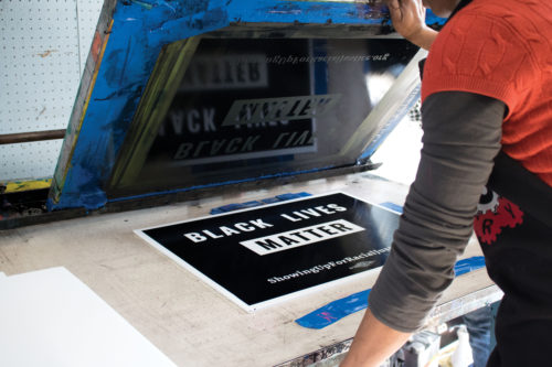 Jen Charles lifts the printing screen to reveal a fully designed sign for an upcoming Black Lives Matter event. Photo by: Michael Evans