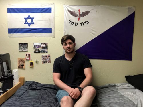Former Israeli Defense Force soldier Yoni Wulf sits on his dorm bed at the University of Arizona in Tucson, Ariz. on October 10, 2019. The purple and white flag on his wall is the flag of his former platoon called the Shaked (acorn) platoon.