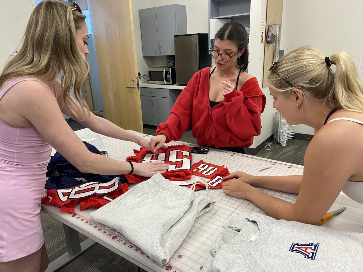 Seniors Ainsley Wells, Jade Danhach and Cora Swanson (left to right) work with scraps of retired football jerseys to plan their design on Thursday, March 19, 2026, in an apparel production class at the University of Arizona.